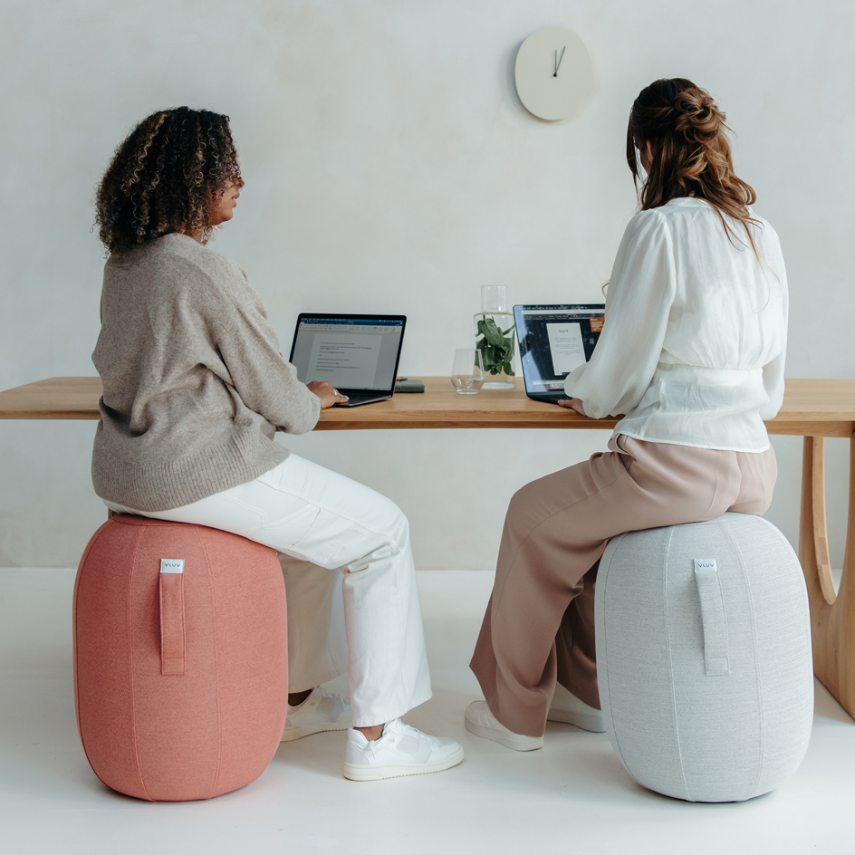 Zwei Frauen sitzen auf roten und grauen Hockern und arbeiten an Laptops.